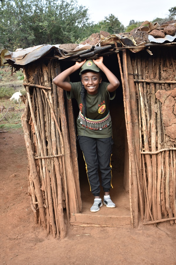 A Maasai girl smiling at the doorway of a traditional homestead